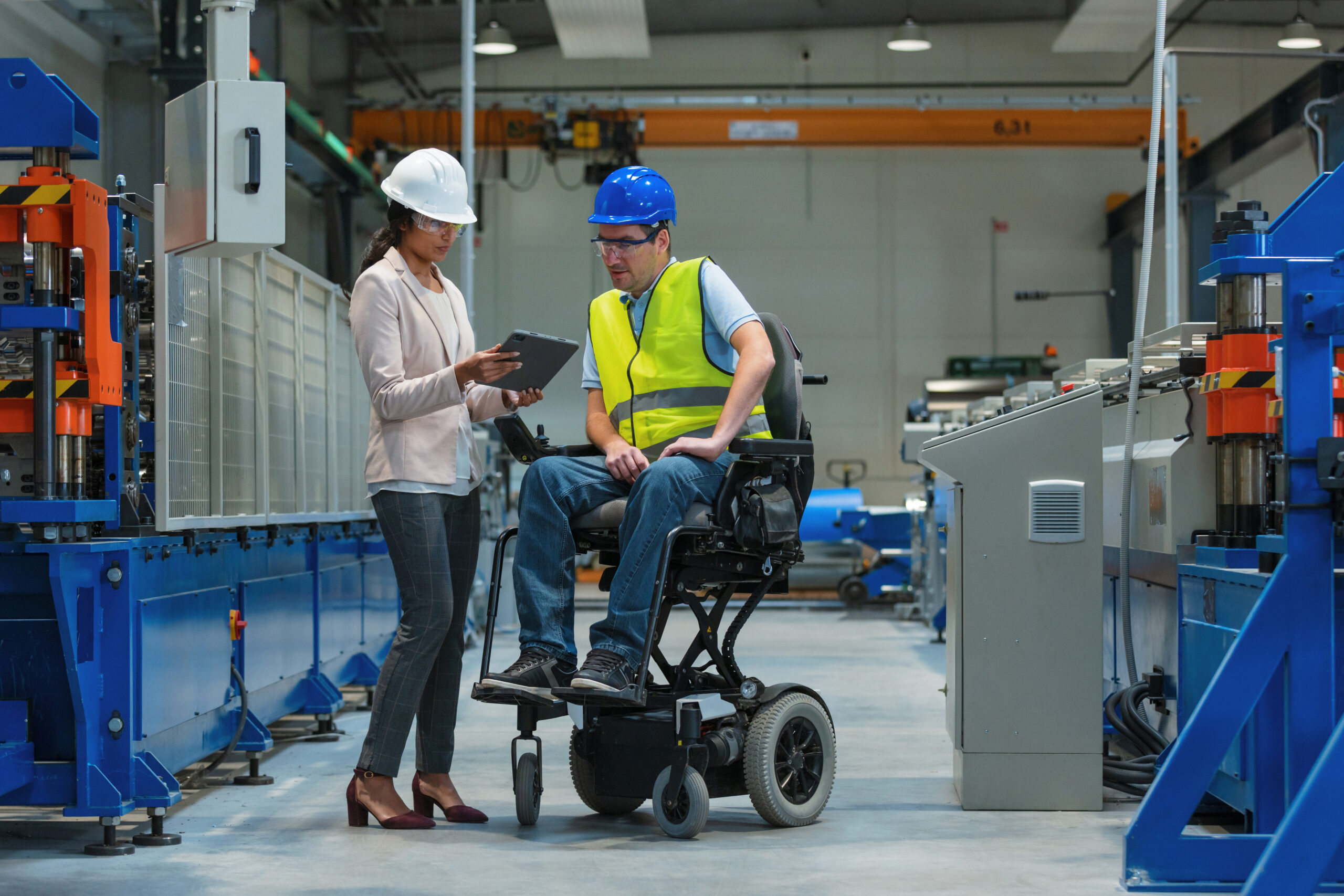 Female manager training a new employee with a disability for a job, explaining work on machines. Industry, inclusion and workplace concept.